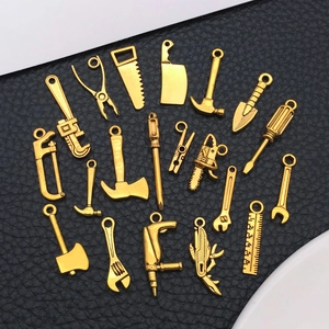Flat lay of diverse gold alloy tool charms featuring mini saws, hammers, and screwdrivers