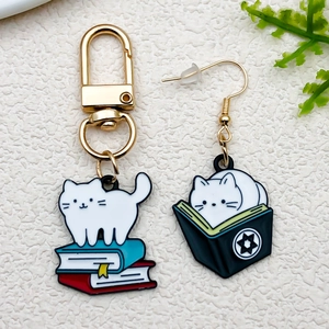 Detailed view of handmade enamel cat charms on a golden keychain and hook earring set