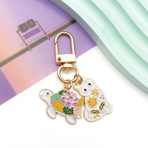 Close-up of golden keychain with enamel cat and turtle charms featuring floral patterns