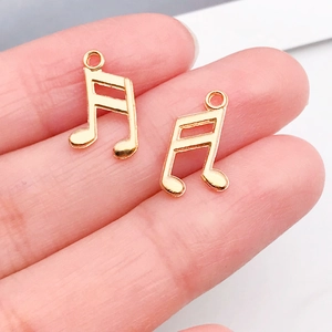 Nahaufnahme kleiner goldener Musiknoten-Anhänger für DIY-Schmuck auf Fingerspitzen