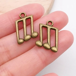 Close-up of bronze musical note pendants held between fingers for DIY jewelry scale