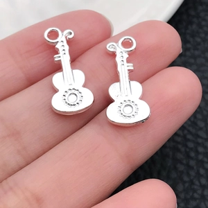 Nahaufnahme von Mini-Silbergitarren-Anhängern für DIY-Schmuck, in der Hand gehalten