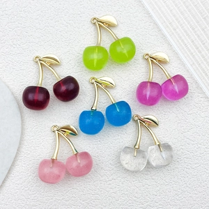 Macro detail of DIY cherry charms in mixed colors with golden leaves on white stone