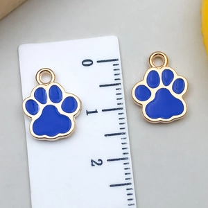Detail showing two blue glitter paw print charms next to a ruler for size reference