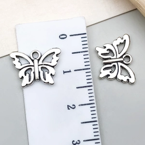 Macro view of two vintage silver-tone hollow butterfly pendants with measurement ruler