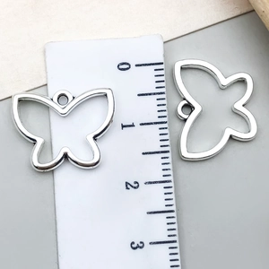Macro view of two vintage hollow silver butterfly charms with ruler showing 20mm width