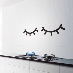 Close-up of matte black eyelash wall stickers on white kitchen tile surface