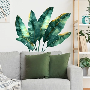 Tropical monstera leaf wall decal with gold foil accents above a gray sofa in a living room