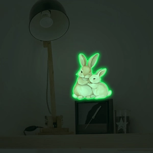 Luminous wall sticker showing two cuddling rabbits glowing green in a dark bedroom