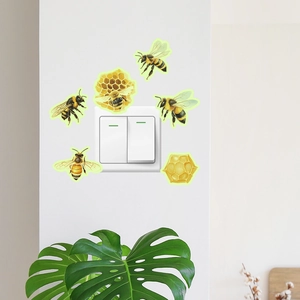 Luminous bee and honeycomb stickers decorating a wall light switch with green leaf accent