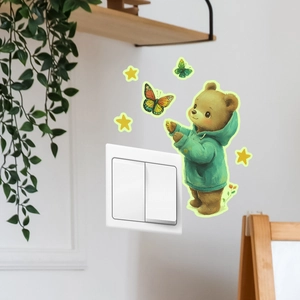 Luminous wall sticker of a brown bear in a green hoodie near a light switch on a white wall