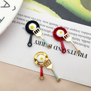 Detailed close-up of mini frying pan and spatula charms for DIY jewelry making