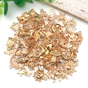 Assorted gold DIY jewelry charms including sun moon and sea animal designs on marble