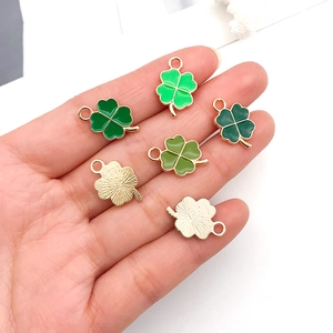 Green enamel four-leaf clover charms with gold plating held by hand for scale