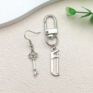 Detailed macro view of silver alloy clover key earring and miniature hand saw tool pendant