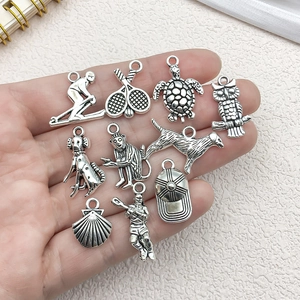 Set of vintage silver alloy charms featuring animals and sports themes held in hand