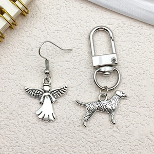 Detailed view of silver angel wing earrings and dog pendant keychain on white texture