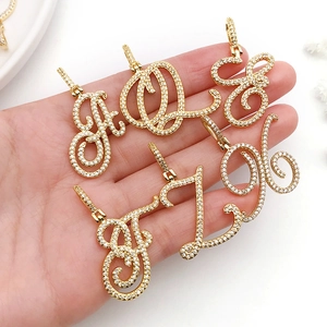 Gold plated hip hop cursive letter pendants with pavé crystals shown on a hand