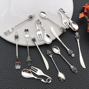 Macro shot of silver alloy mini cutlery charms with crown details on a black texture