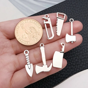 Lot de six pendentifs outils en métal argenté avec scies et haches et une pièce de monnaie