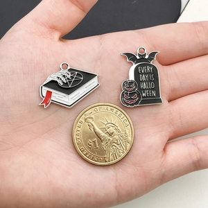 Halloween enamel charms with magic book and tombstone motifs shown next to a coin