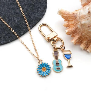 Detail of blue enamel flower necklace and guitar glass keychain charms in gold
