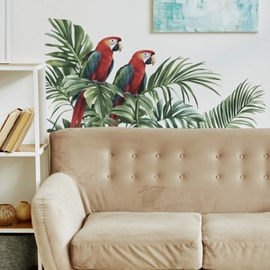 Tropical wall sticker with red macaws and green leaves on white wall above a sofa