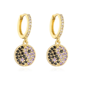 Gros plan de boucles d'oreilles créoles dorées avec pendentifs yin yang en pierres violettes