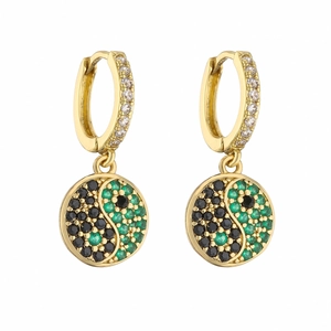 Détail de créoles dorées avec pendentifs yin yang et zircons verts sertis micro-pavé