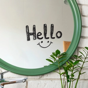 Green framed round wall mirror with Hello text and smiley face decal on brick wall