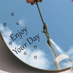 Golden round wall mirror with Enjoy Your Day text reflecting blue sky and dried rose