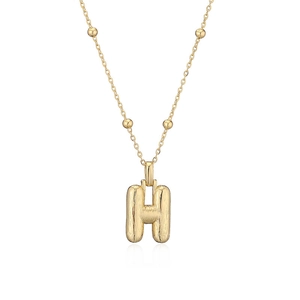 Gros plan du pendentif lettre H doré montrant la texture en métal brossé fin