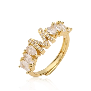Dettaglio di un anello dorato con lettera M con zirconi lucidi e fascia aperta regolabile