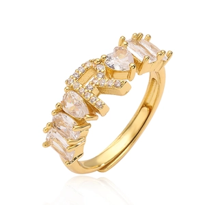 Dettaglio dell'anello dorato con lettera R e zirconi a forma di cuore e a goccia