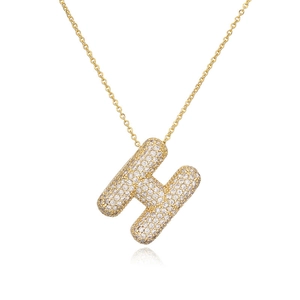 Dettaglio del ciondolo dorato con lettera H e pietre di zirconio cubico micro-pave