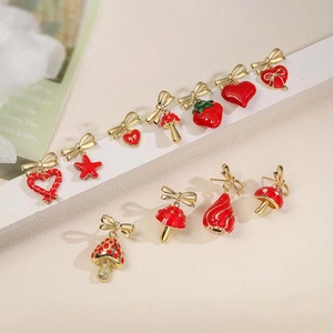 Dettaglio di orecchini placcati oro con ciondoli smaltati fragola fungo e a cuore
