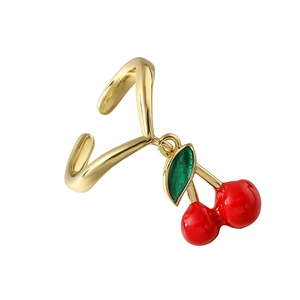 Dettaglio di un ear cuff dorato a forma di ciliegia con smalto rosso e foglia verde