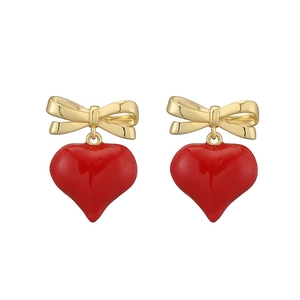 Dettaglio di orecchini a cuore in smalto rosso con fiocco dorato e stile vintage dolce