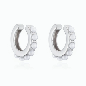 Macro detail of silver C-shaped ear cuffs set with glossy white pearls and metal base