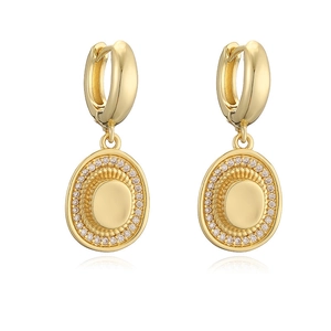 Macro detail of gold huggie hoop earrings with oval sunburst charms and white zircon pavé