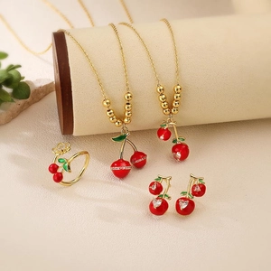 Detail of red enamel cherry jewelry set with necklaces, earrings and open ring in gold finish