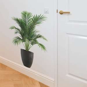 Close-up of artificial tropical plant in a black textured pot with a white wall backdrop