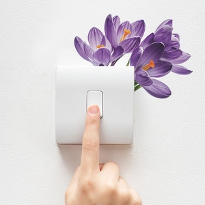 Detail showing a hand pressing a white light switch decorated with purple flower stickers