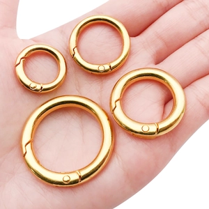 Set of four gold metal spring o-rings for bag hardware in various sizes held in hand