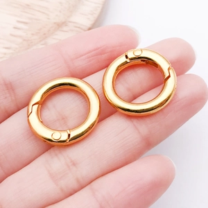 Detail showing a pair of gold round spring gate rings for bags held by fingers for scale