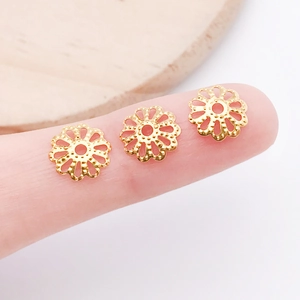 Detailed macro view of small 7mm gold hollow flower bead caps held on a fingertip