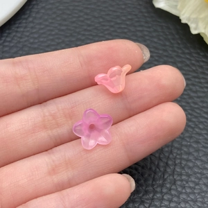 Vista macro de pequeñas cuentas de flores de acrílico traslúcido en un dedo para joyas DIY