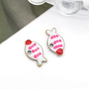 Detail van twee geëmailleerde visvormige bedeltjes met roze stippen voor DIY-sieraden