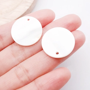 Vue macro de pendentifs ronds en nacre blanche tenus à la main pour bijoux artisanaux