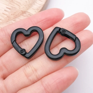 Close-up of heart-shaped matte black alloy spring clasp held by fingers for size